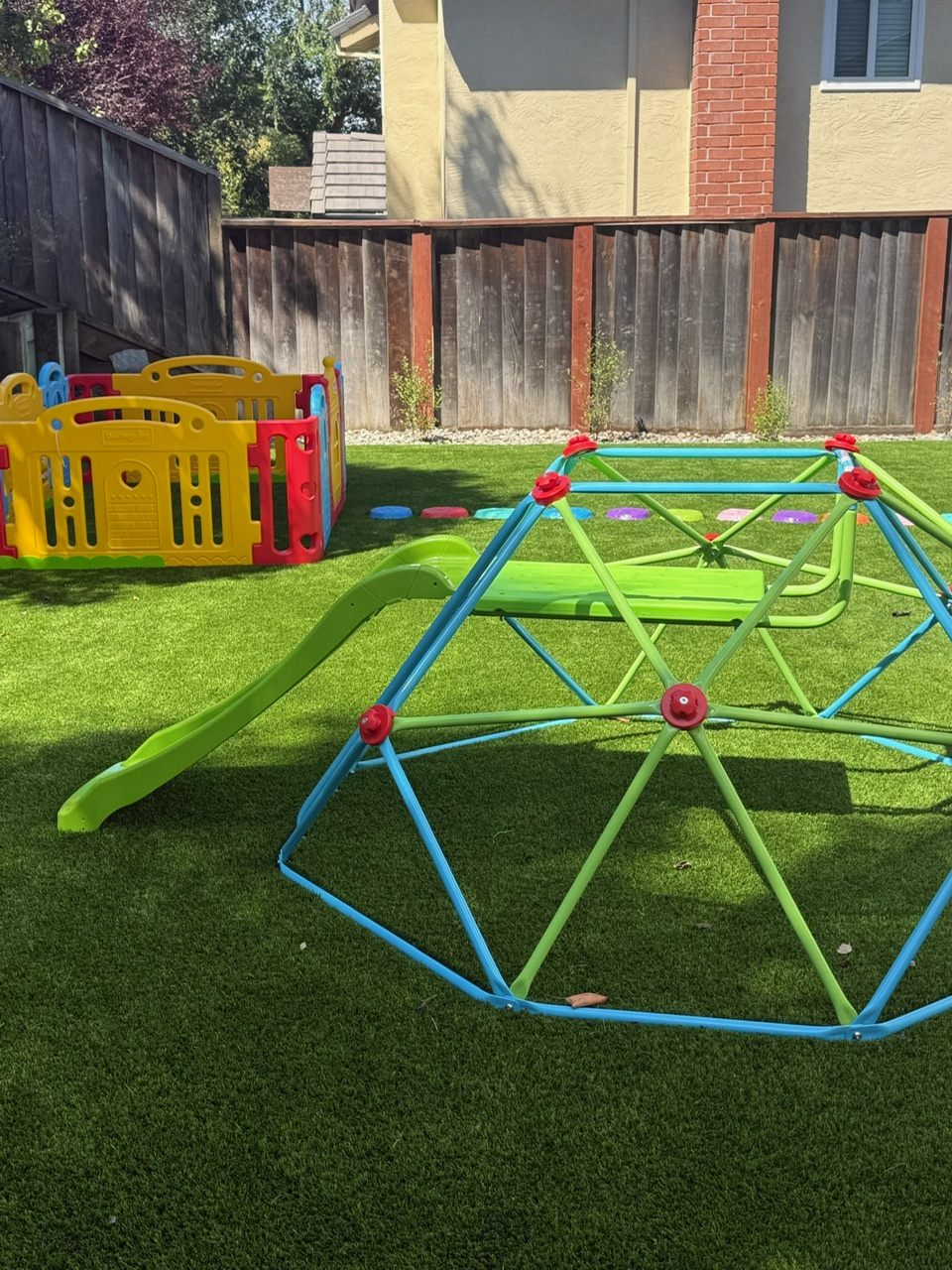 Our backyard play area: climbing dome with slide, stepping stones, and a gated play space on soft turf
