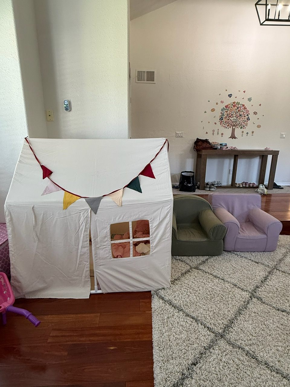 A fabric play house with bunting next to two child-size armchairs